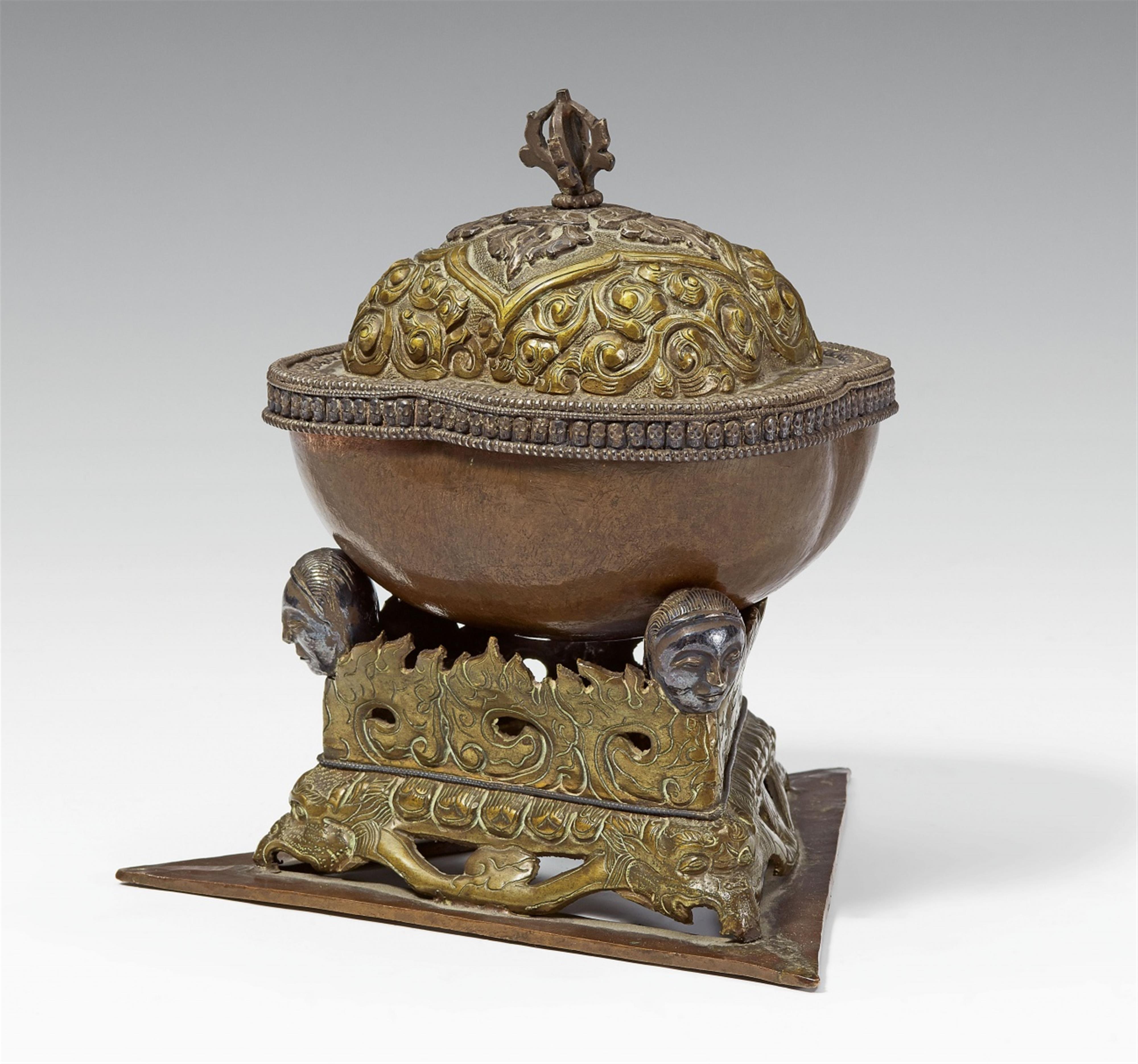 A Tibetan copper kapala with a brass lid and stand with silver details - image-1