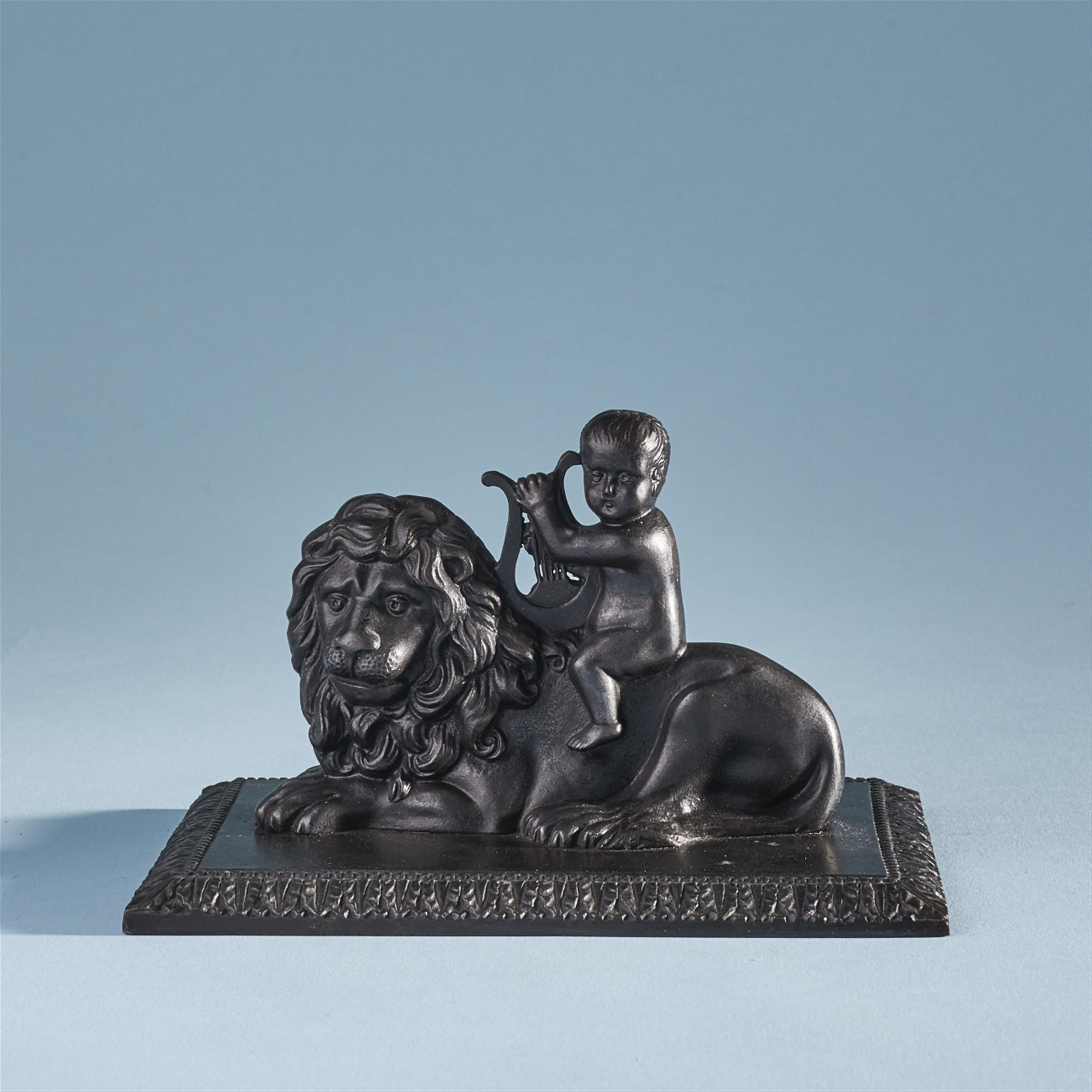 A cast iron paperweight formed as Cupid riding a lion - image-1